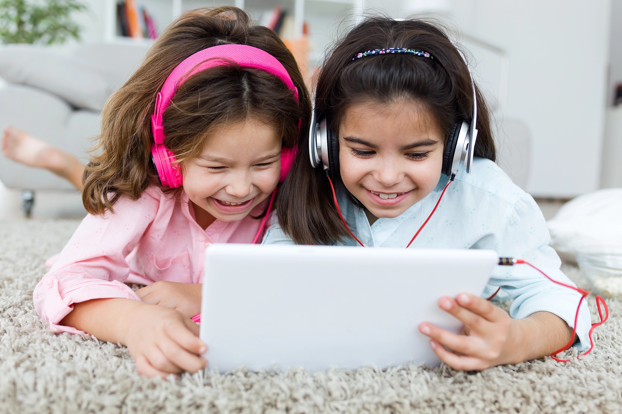 Two girls laughing at a tablet with headphones on